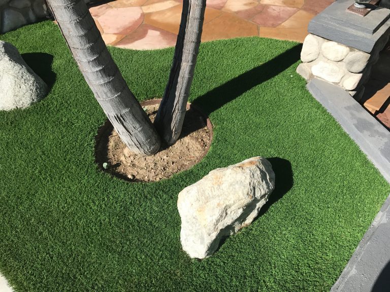 Synthetic turf fitted neatly around a palm tree and boulder