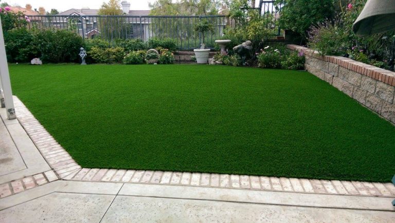 Wide backyard artificial lawn edged with pavers