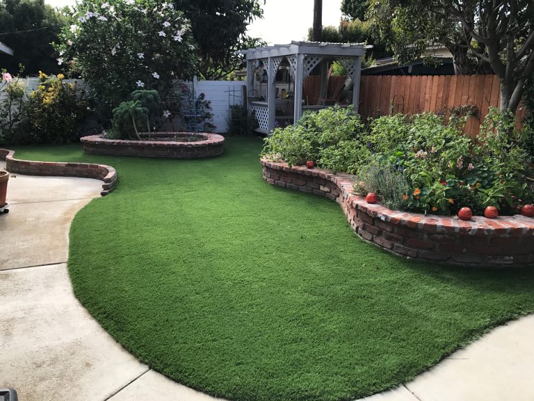 Curved artificial grass lawn bordered by a brick planter and flower garden