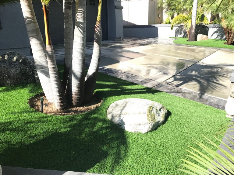 Synthetic turf around palm trees and a boulder beside a patio